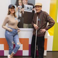 A grandfather and granddaughter pose next to their photo of each other in the exhibition