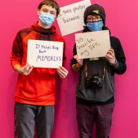 Two teens posing in the exhibition with written signs explaining their reasons why they take photos