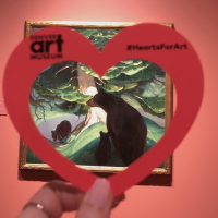 Hand holding a paper heart in front of the artwork "Black Bears" by Herbert Dunton at the Denver Art Museum.