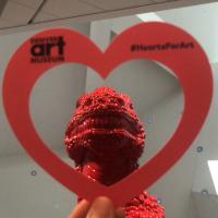 Hand holding a paper heart in front of the statue "Made in China" at the Denver Art Museum.