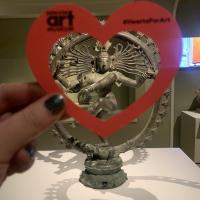 Hand holding a paper heart in front of the statue "Shiva Nataraja"