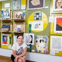 Student posing in front of their artwork on display in the showcase