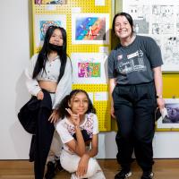 Students posing in front of their artworks on display in the showcase