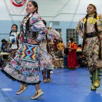 Two women in traditional Indigenous clothing performing for a crowd at Powwow 2021