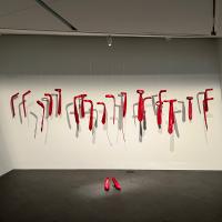 Pair of heels made out of lipstick wax on the ground, surrounded by suspended ties and an unfolded hanger, both also made out of lipstick wax. 