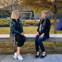 two women sit on a bench outside the museum modeling a coat and a sweater by Betsy Wiersma