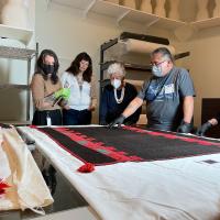 people around a table with a black and red texile. A man points at the fabric