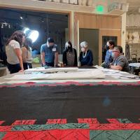 DAM staff and Acoma cultural advisors looking at a large cloth on a table in the textile conservation lab