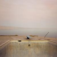 Photograph of a diving board, water, and light grey sky