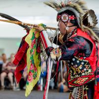 Man performing with a flute while dressed in traditional Native American wear 
