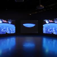 Three large projection screens displaying images of space