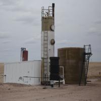 A seemingly abandoned industrial structure stands rusting in the middle of a yellow prarie.
