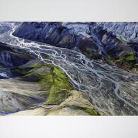 Colorful aerial photo graph of a fertile glacial delta cut between two ridgelines. The lines of the delta frequently branch and rejoin each other evoking the image of a braid.