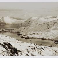 A sepia-like photograph of a bay with ships in the middle of a frozen hilly landscape.