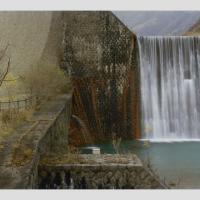 Water flows over a brickwork dam. Bright streaks of ruddy brown run vertically to the side of the waterfall, implying that water has run over that part of the dam wall in the past.