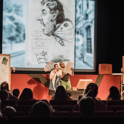 actors on stage in front of screen showing a caricature drawn by Claude Monet