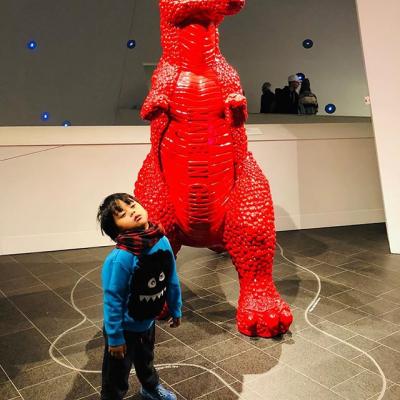 Kid posing in front of red dinosaur sculpture