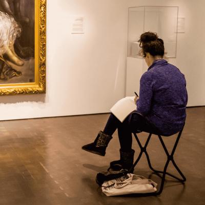 Person sitting in a gallery at the Denver Art Museum writing in a journal