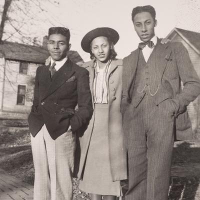 three people, 2 men with a woman between them photographed outside