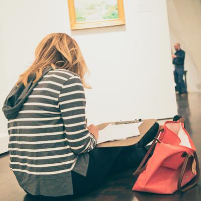 Woman sitting and drawing in front of a painting