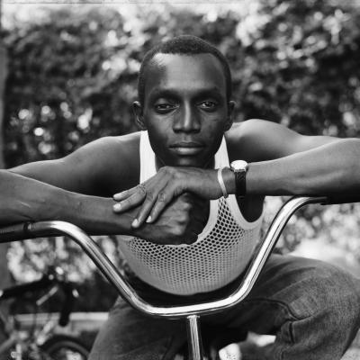 Black and white photograph of a young black man resting on the handles of his bike