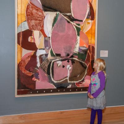 Child standing in front of large pink and orange abstract painting of Sweet Potatoes at the Table by Roberto Juarez, 1987