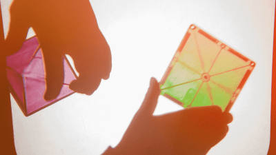 A child's hand playing with shapes, light, and colors