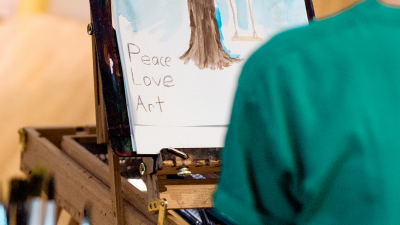 Child painting with "Peace Love Art" written in bottom left-hand corner