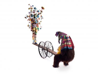 a seesaw with a mannequin with vintage toys on it on one side and a hairy figure on the other side