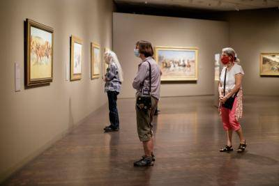 Three masked women looking at an artwork while social distancing