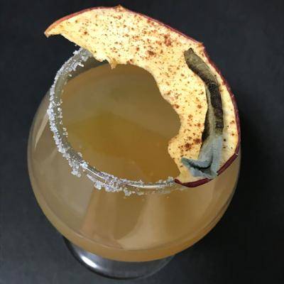 a glass filled with a cocktail with an apple slice on top