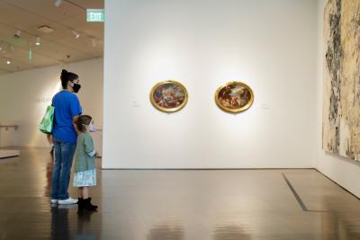 Mother and daughter in masks admiring tall painting