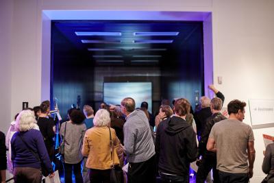 Visitors gather in the museum to look at a digital projection