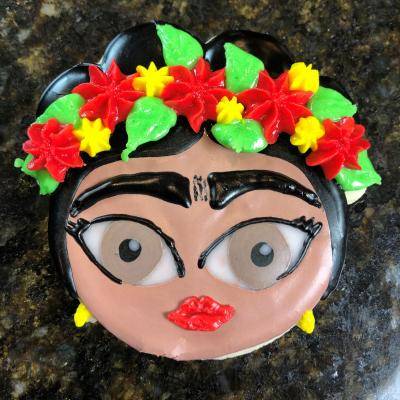 a cookie that looks like Frida Kahlo's head with red and yellow flowers in a flower crown