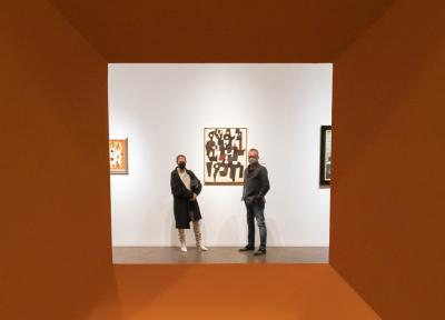 Red wall with a cutout in the center showing visitors looking at a painting.