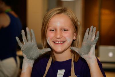 Young girl smiling with her hands covered in clay