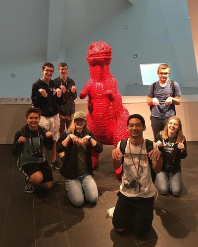 Group of students posing next to large red dinosaur sculpture