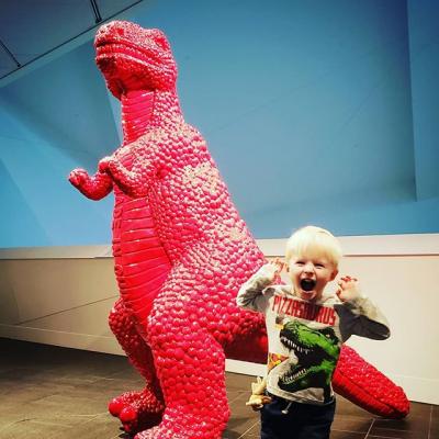 A kid roaring in front of a large red dinosaur sculpture