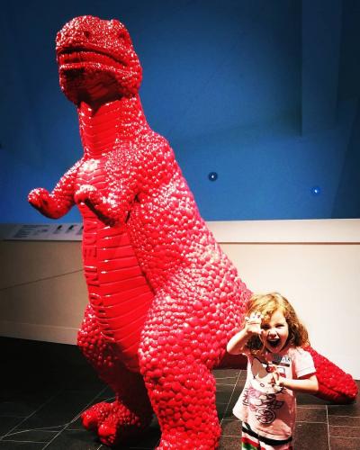 Young girl posing in front of large red dinosaur sculpture