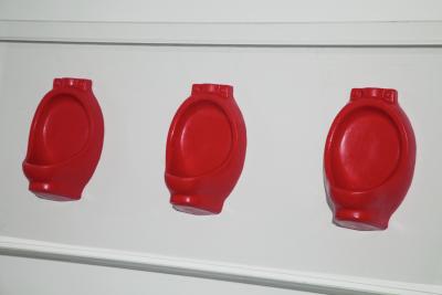 Row of three miniature red wax urinals affixed to a white wall.