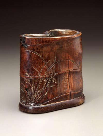Dark brown stained bamboo brush pot. The pot is oddly shaped like a cylinder that has been pinched in the middle.