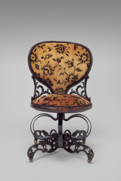 Yellow upholstered chair with a floral print. The chair is made of carved wood and rests on a spring steel base.