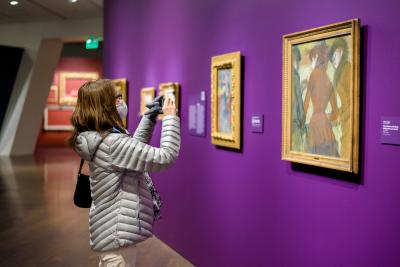 Masked woman taking a photo of a painting.