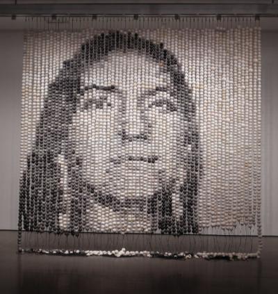 Large sculptural installation comprised of two-inch clay beads hung on strings from the ceiling to the floor. Together the beads create an image of a woman’s face in black and white.