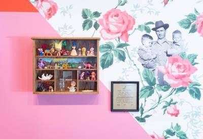 Wall of brightly colored flowered wallpaper and a display of kitschy knicknacks