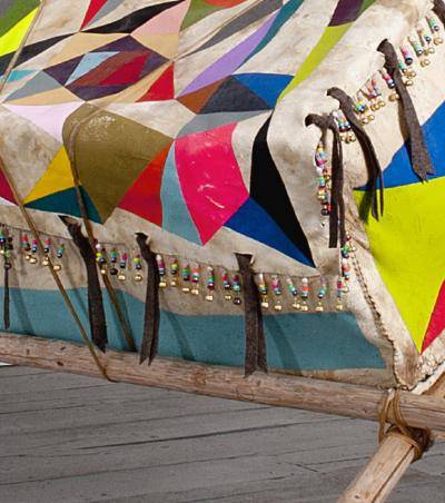 Detail of oversized rawhide box with painted geometric shapes in bright colors, on repurposed tipi poles