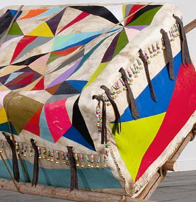 Detail of oversized rawhide box with painted geometric shapes in bright colors, on repurposed tipi poles