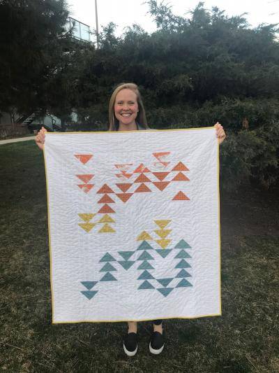 Kati Woock standing outside holding up a quilt she made