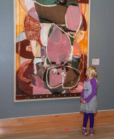 Child standing in front of large pink and orange abstract painting of Sweet Potatoes at the Table by Roberto Juarez, 1987