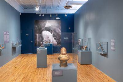 Gallery view of the Rhythm and Ritual exhibition with ancient musical instruments inside glass cases and a picture of a musician on the wall